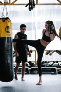 A woman practicing kickboxing with a trainer in a gym setting, focusing on technique and fitness.